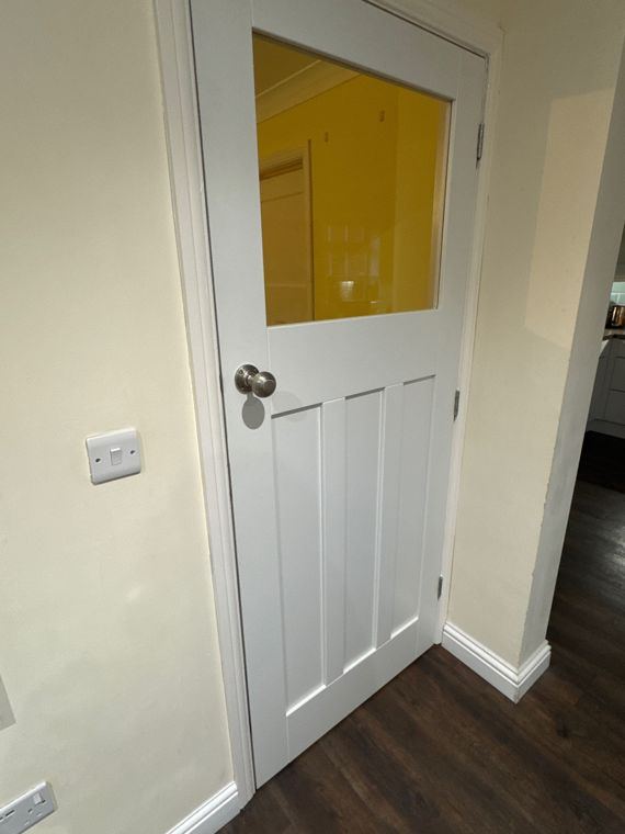 A white half-glazed panel door with a round metal knob, skirting fitted below