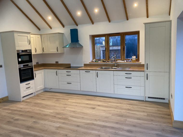 A shaker-style kitchen under a vaulted beamed ceiling, wood-effect worktops and floor