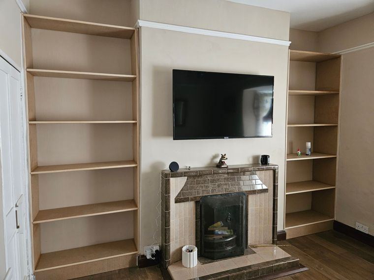 Unpainted shelving fitted into both alcoves beside a tiled fireplace