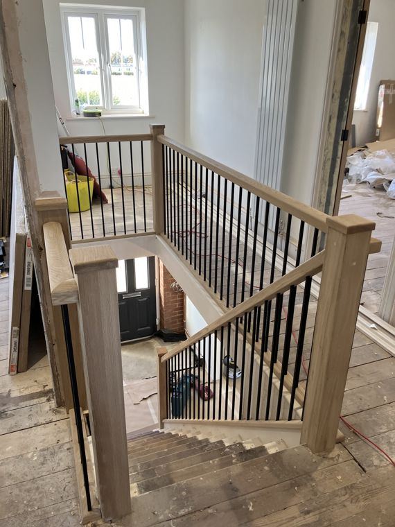 A new balustrade with black spindles round a stairwell, the landing still bare boards