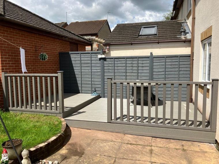 A raised grey deck on two levels with a spindle balustrade beside a patio