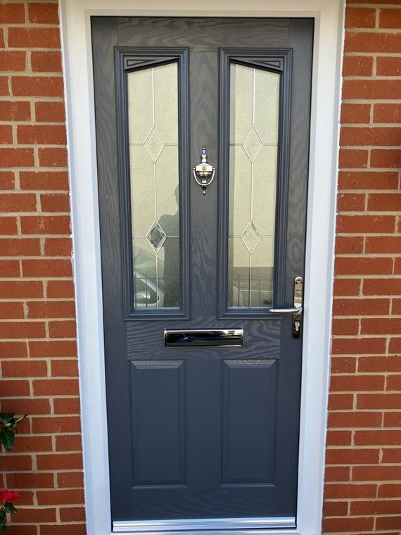 A grey front door with patterned glazed panels set in a brick opening