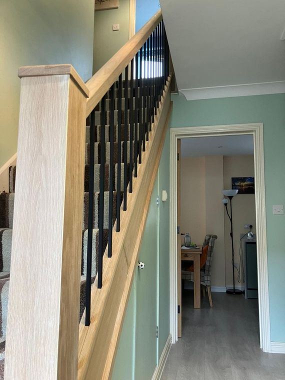 A timber newel and handrail with black spindles beside a carpeted staircase