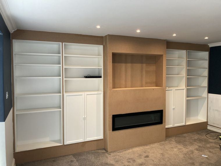 A wall of shelving and cupboards, the centre fire surround still bare board