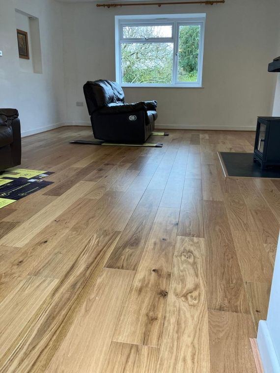 A wide-plank wood floor laid through a lounge, furniture on protective boards